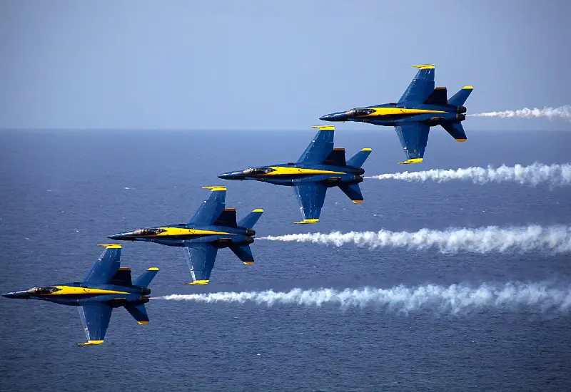 Photograph of the Blue Angels flying side-by-side over the ocean with smoke trails.