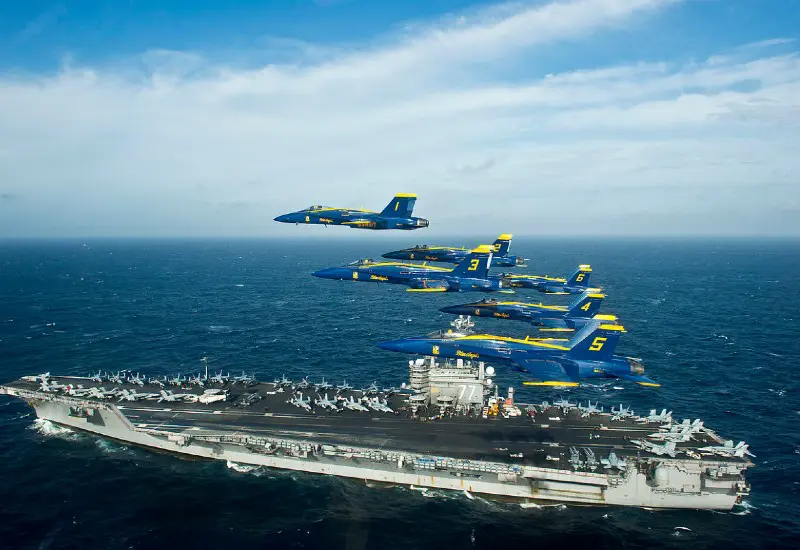 Blue Angels flying over ocean with carrier ship in the background.