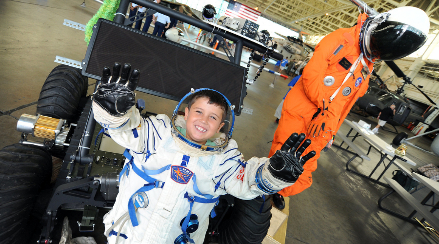 Young boy dressed in a spacesuit on a moon rover.