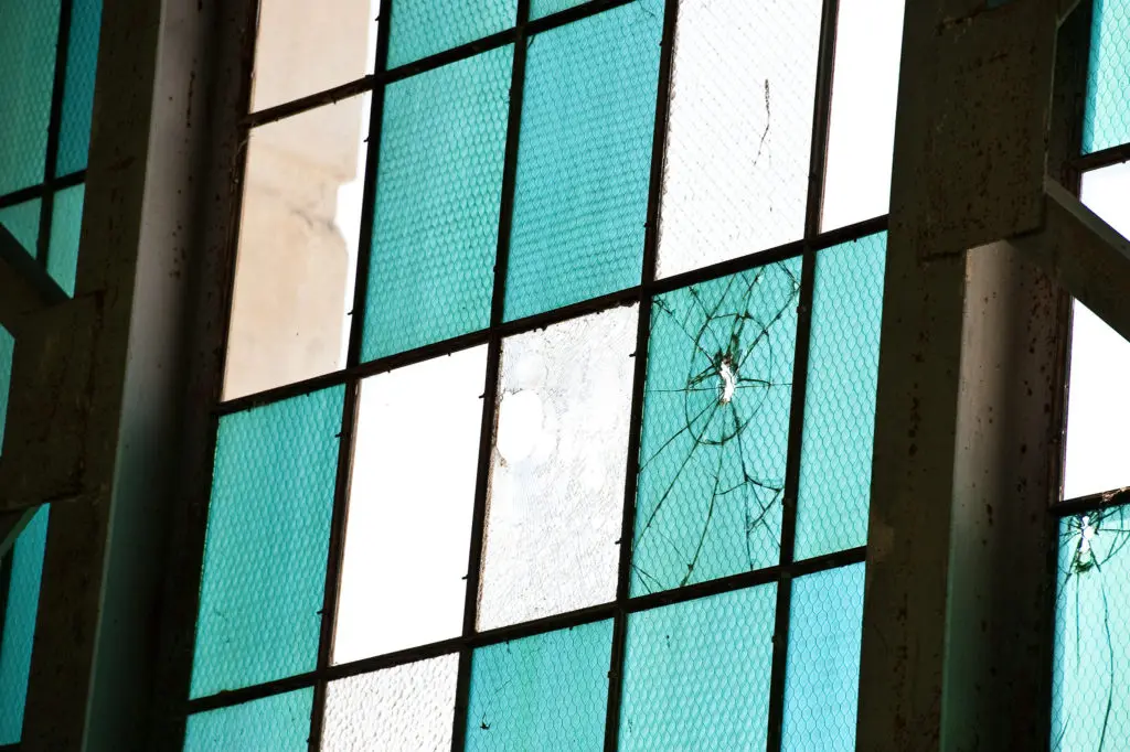 Photograph of bullets holes in the original glass panes of the windows in Hangar 79. Blue and clear panes set in metal doors.