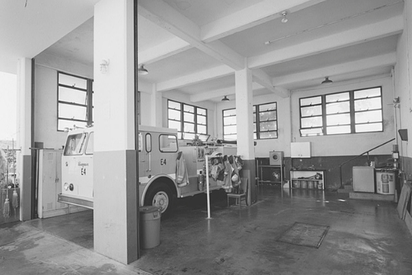 Black and white photograph of the fire station garage in the Ford Island Control Tower. Concrete with windows and a parked car.