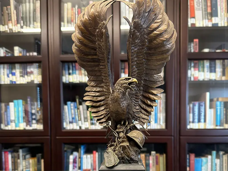 Photograph of bronze eagle statue in front of book cases inside the Pearl Harbor Aviation Museum Library/Archive.