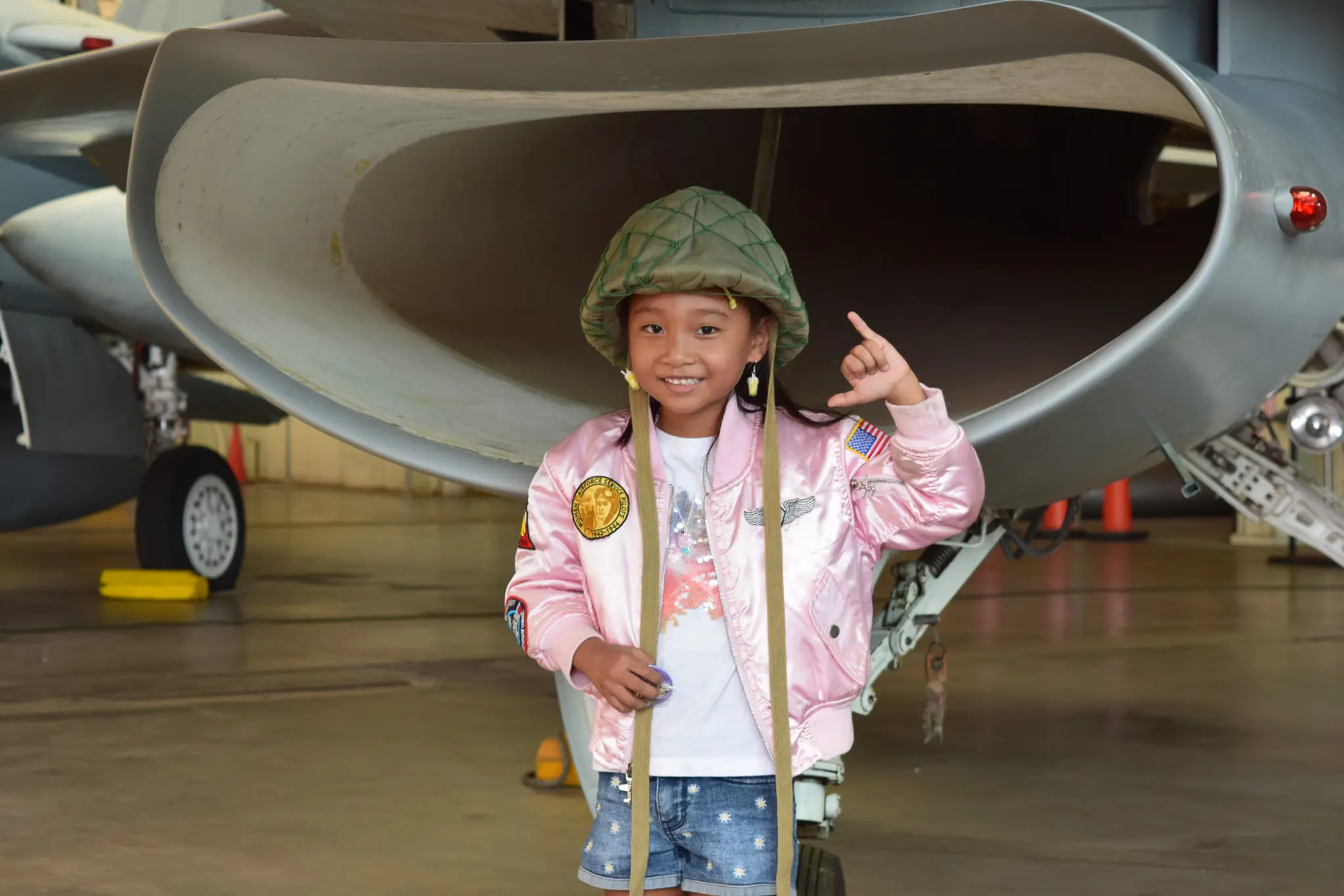 Small girl standing in front of a plane wearing a helmet