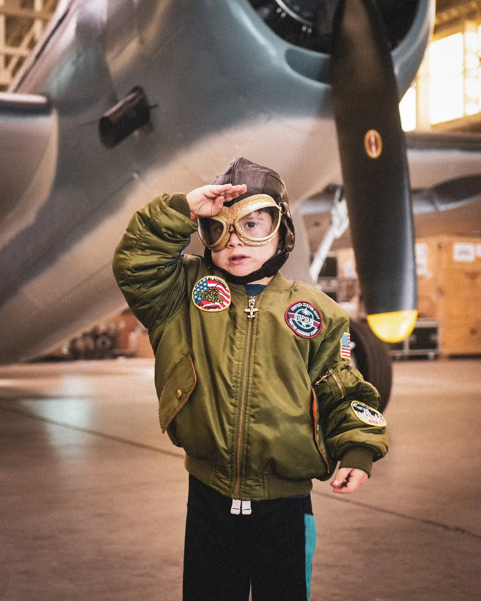 Boy dressed up saluting with a plane behind him