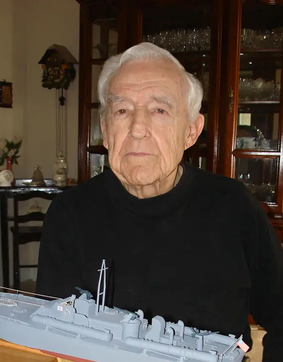 Photograph of an older Jack Sheretz smiling while posing in front of model ship.
