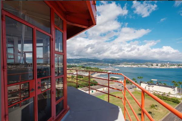 Photograph of glass room a top the Ford Island Control Tower. Red doors lead out to the balcony of the tower with views of the harbor below.